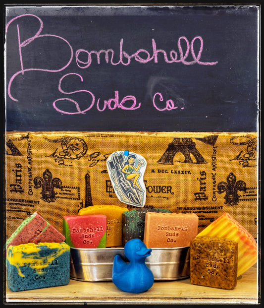 Bombshell Suds Co handmade soap bars on display with brand chalkboard sign