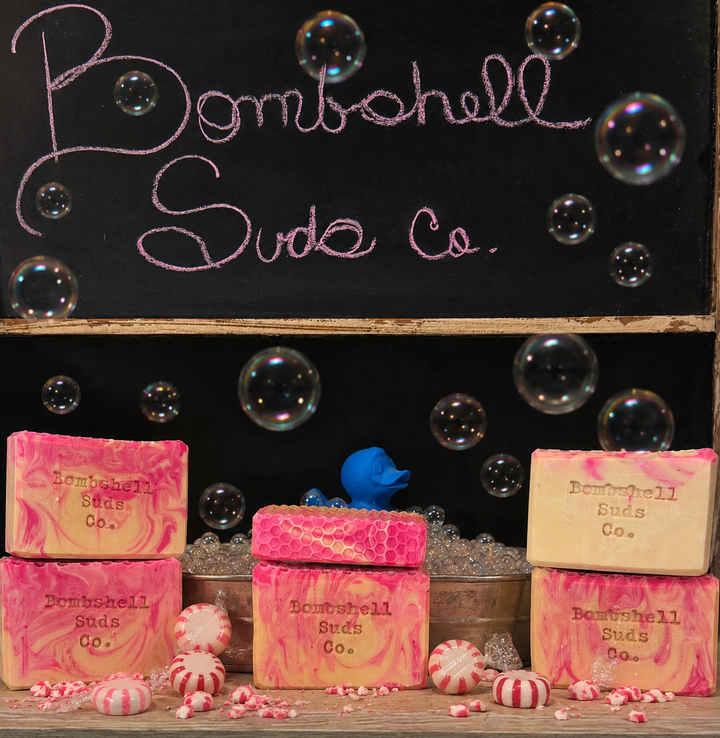 Bombshell Suds Co. soaps with decorative elements on a black background with bubbles.