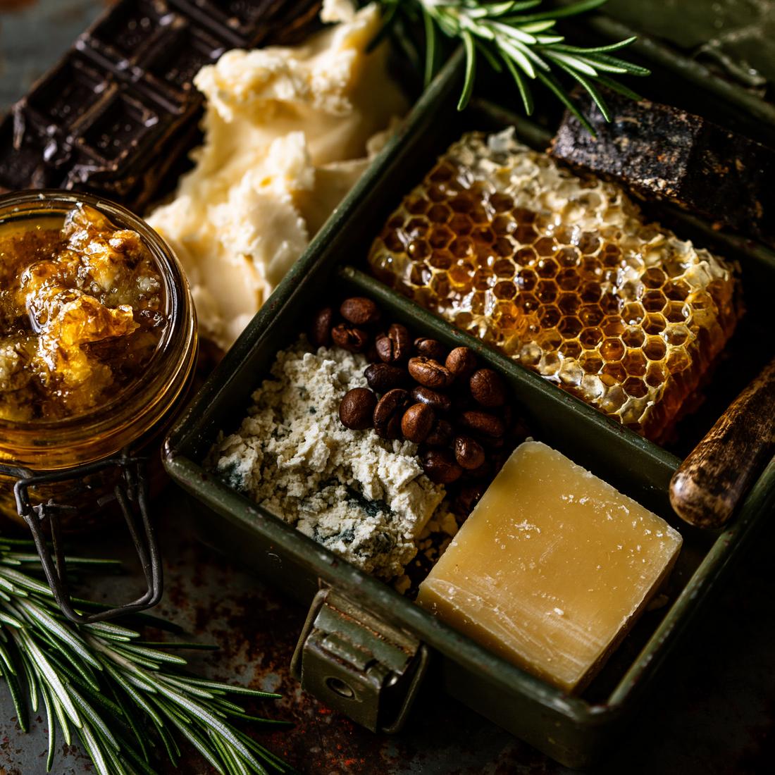 Raw Bombshell Suds ingredients packed in an olive drab ammo can: honeycomb, raw honey, shea butter, tallow, coffee beans, colloidal oats, rosemary